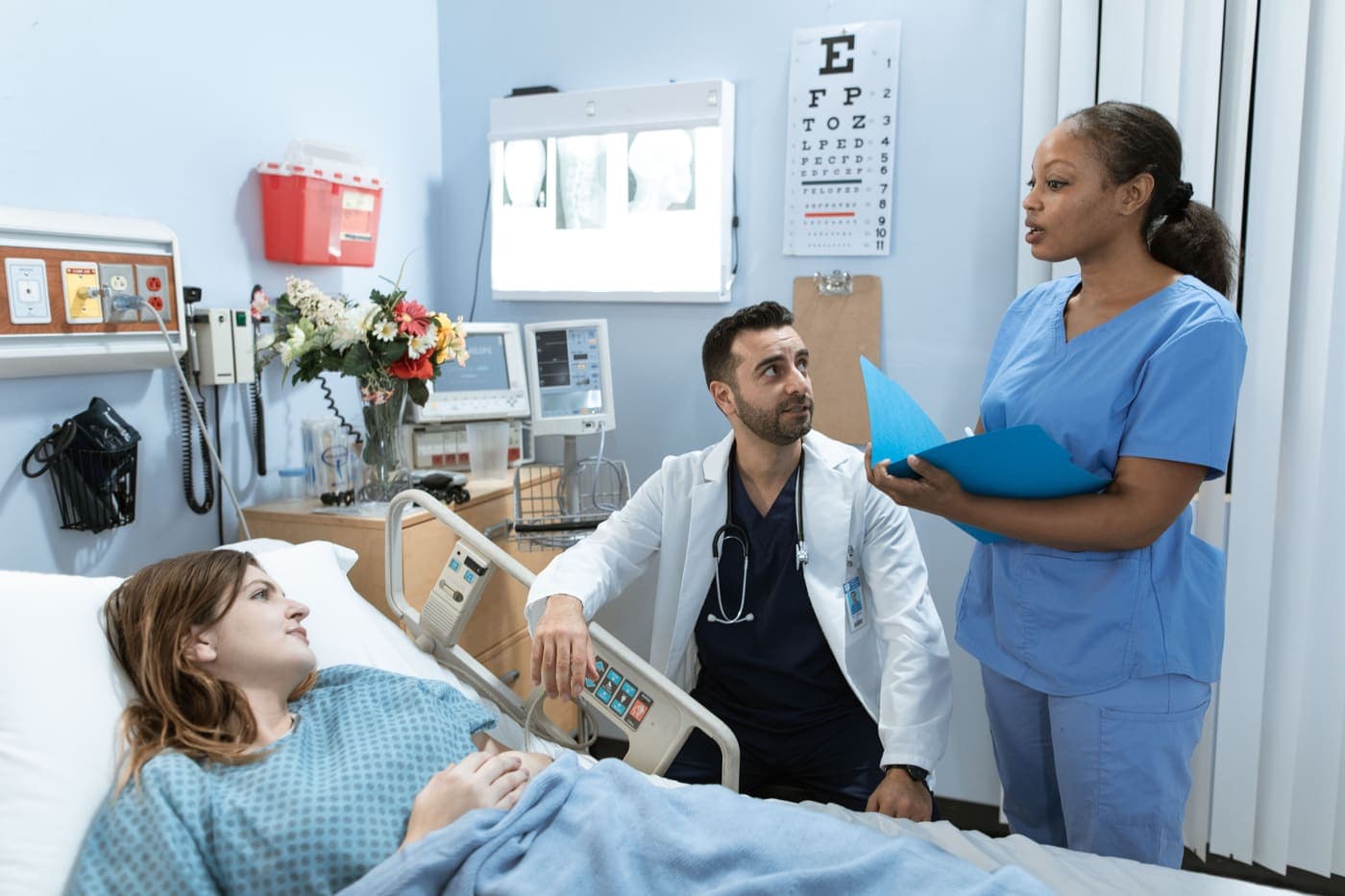 A doctor and a nurse talking with a patient at her hospital bedside.